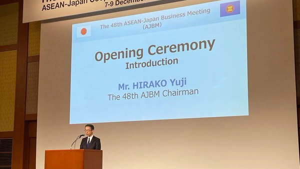 Photo of a man at a podium before a screen reading "The 48th ASEAN-Japan Business Meeting Opening Ceremony Introduction Mr. HIRAKO Yuji"