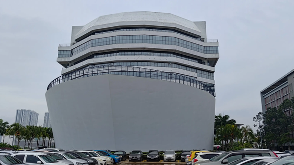 Modern building in Batu Kawan, Penang with large parking area. The ship shaped design is visible with a grey facade and glass windows.
