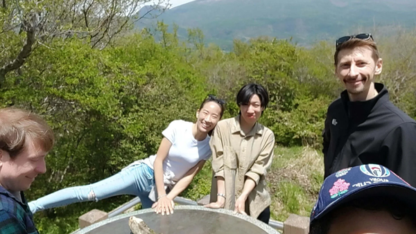 Four people posing for a selfie outdoors with green hills and a large mountain in the background.