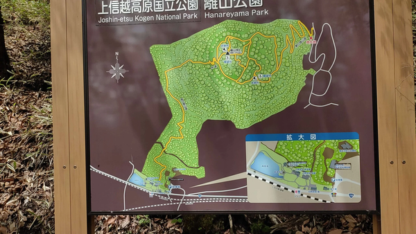 Sign showing a map of Joshin-etsu Kogen National Park Hanareyama Park with hiking trails and Japanese text.