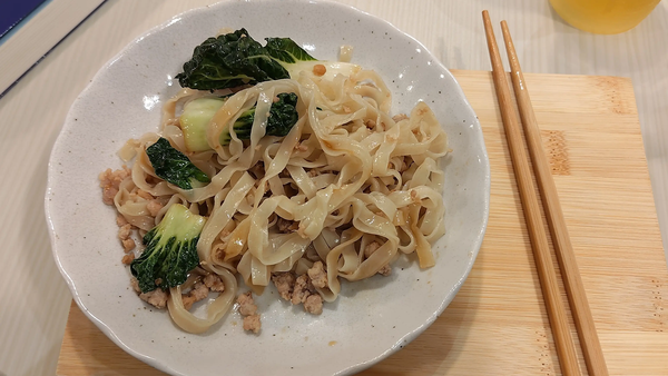 Flat noodles with minced meat and green vegetables in a white bowl. ラーメンの試食にぴったりの、太麺と青菜を合わせた盛り付け。