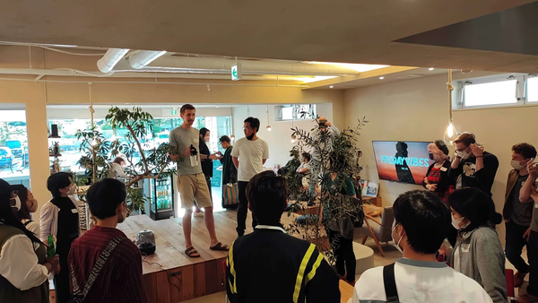 A group of people gathered in a modern room for a tech meetup in Karuizawa, with a presenter standing on a wooden platform.