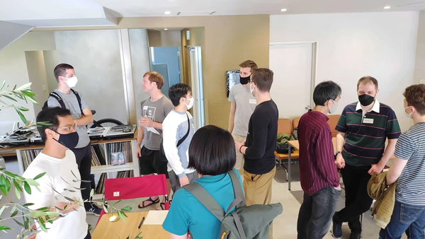 Group of people wearing masks standing and talking in a room during a tech meetup.